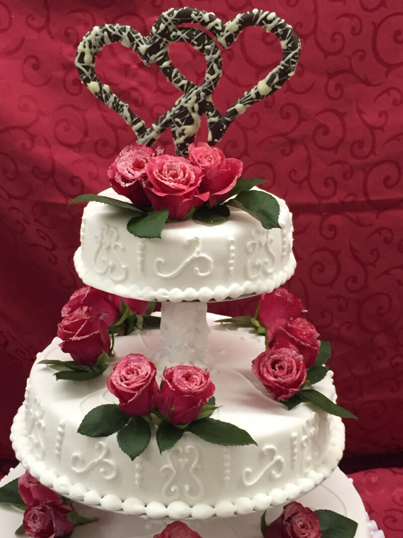 Hochzeitstorte weiss mit echten roten Rosen und zwei Schokoladenherzen oben